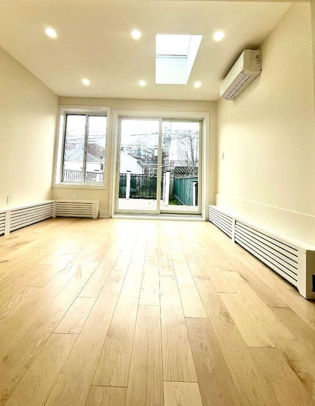 unfurnished room featuring radiator heating unit, a skylight, light hardwood / wood-style flooring, and a wall mounted AC