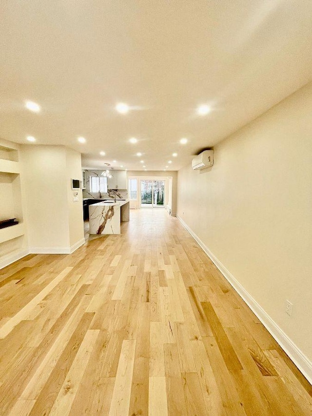 unfurnished living room with built in shelves, light wood-type flooring, and a wall mounted air conditioner