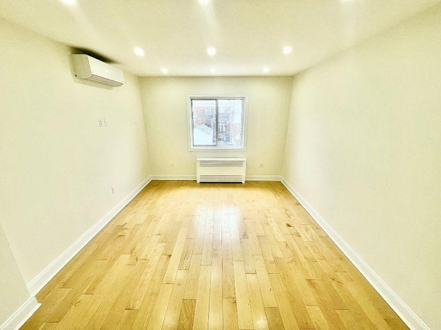 empty room featuring an AC wall unit and light wood-type flooring