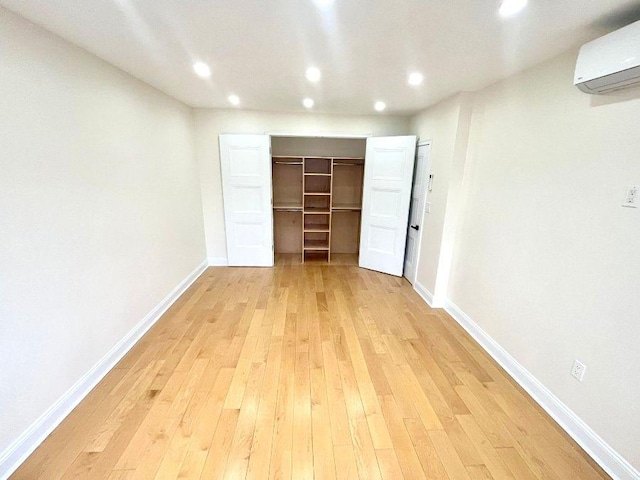 unfurnished bedroom featuring a wall unit AC, a closet, a spacious closet, and light hardwood / wood-style flooring