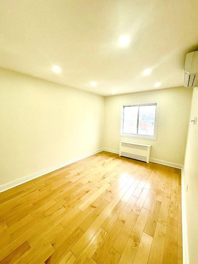 spare room with a wall mounted AC, light hardwood / wood-style flooring, and radiator heating unit