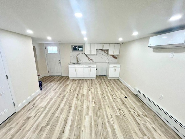 clothes washing area featuring baseboard heating, an AC wall unit, light hardwood / wood-style floors, and sink