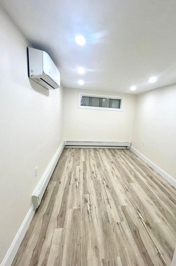 basement with a baseboard heating unit, an AC wall unit, and light hardwood / wood-style flooring