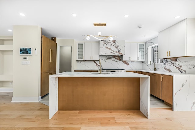 kitchen with white cabinets, light wood-type flooring, an island with sink, and high quality fridge