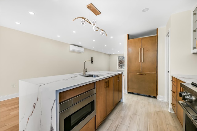 kitchen featuring a kitchen island with sink, hanging light fixtures, light hardwood / wood-style flooring, an AC wall unit, and sink