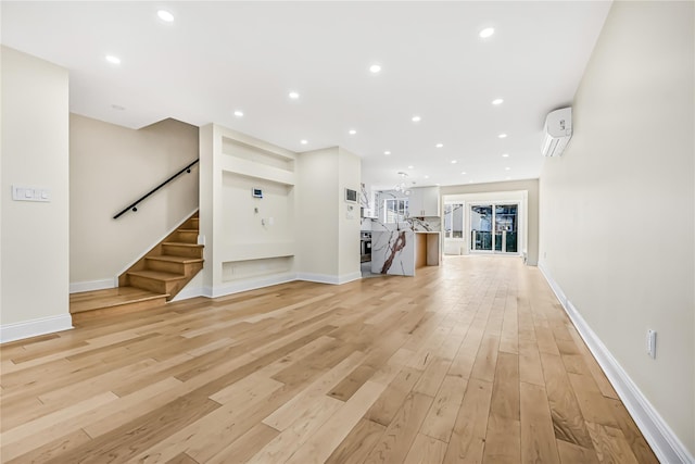 unfurnished living room featuring light wood-type flooring, built in features, and a wall mounted air conditioner