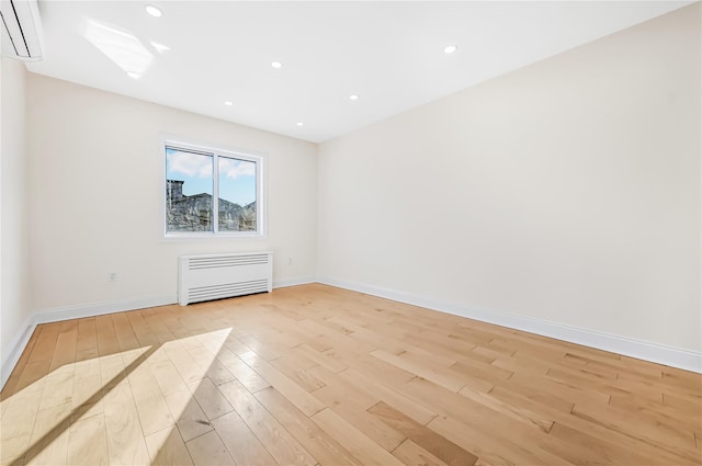 spare room featuring light hardwood / wood-style floors, radiator heating unit, and a wall unit AC