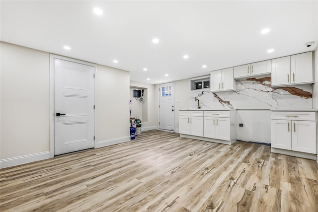 kitchen featuring light stone countertops, backsplash, white cabinets, and light hardwood / wood-style flooring