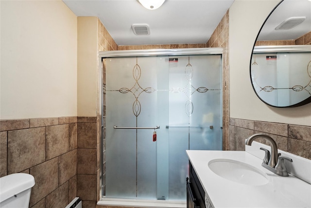 bathroom featuring vanity, toilet, tile walls, and a shower with shower door