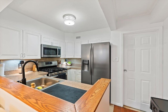 kitchen featuring appliances with stainless steel finishes, white cabinetry, sink, wooden counters, and kitchen peninsula