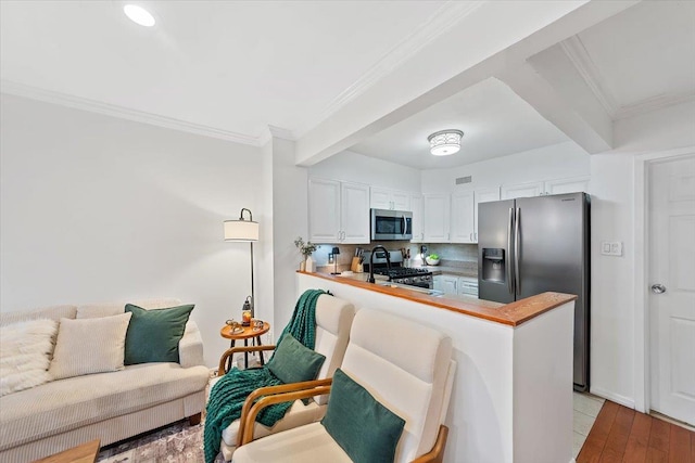 kitchen with appliances with stainless steel finishes, wood counters, white cabinets, backsplash, and kitchen peninsula