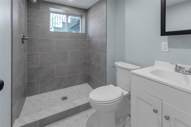 bathroom with toilet, a tile shower, and vanity