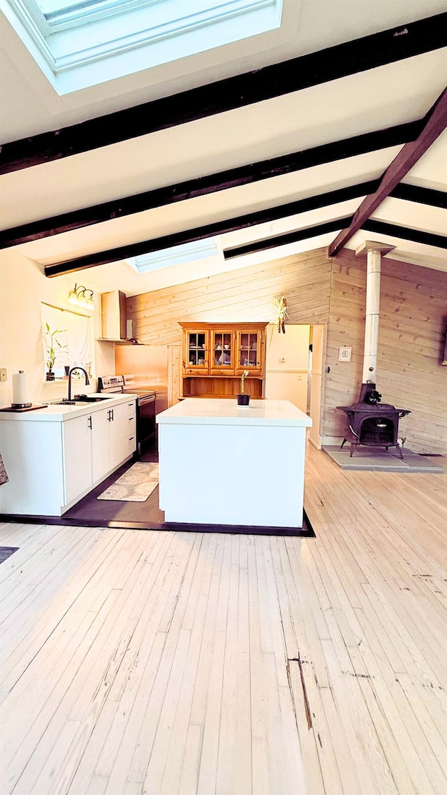 unfurnished living room with vaulted ceiling with skylight, sink, wood walls, and light hardwood / wood-style floors