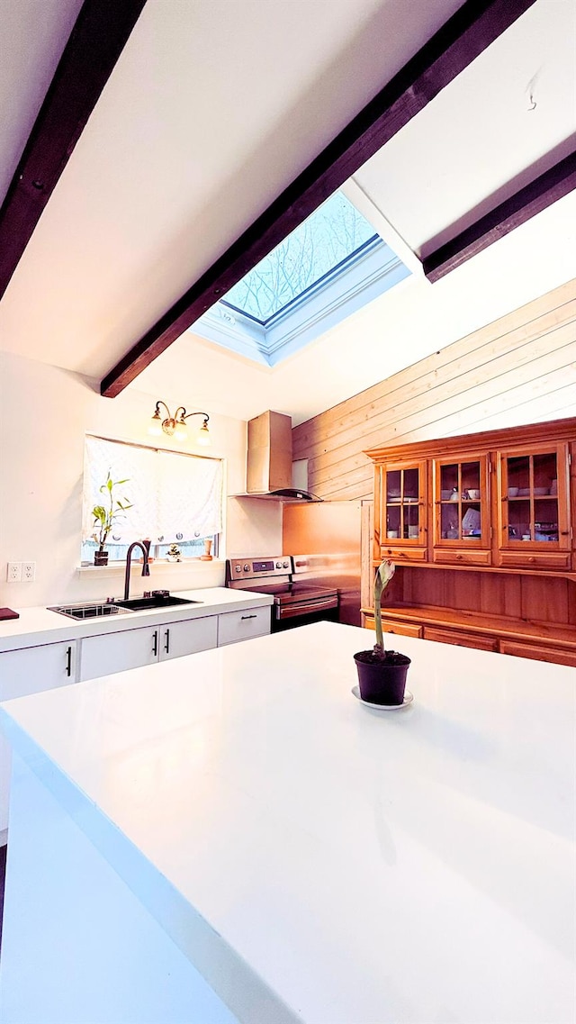 kitchen with wall chimney exhaust hood, white cabinetry, a skylight, sink, and electric range