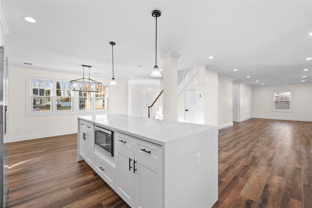 kitchen with a kitchen island, stainless steel microwave, white cabinets, dark hardwood / wood-style flooring, and hanging light fixtures