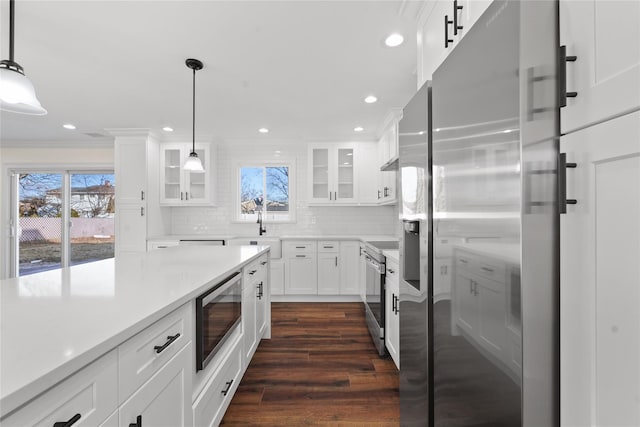 kitchen with dark wood-type flooring, appliances with stainless steel finishes, hanging light fixtures, tasteful backsplash, and white cabinets