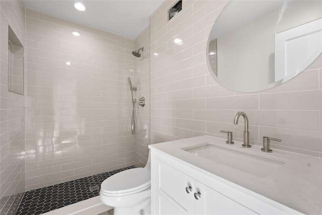 bathroom featuring vanity, a tile shower, tile walls, and toilet