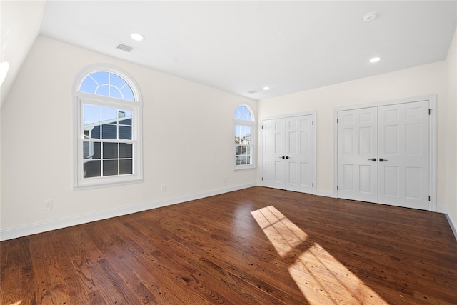 unfurnished bedroom with dark hardwood / wood-style flooring, vaulted ceiling, and multiple closets