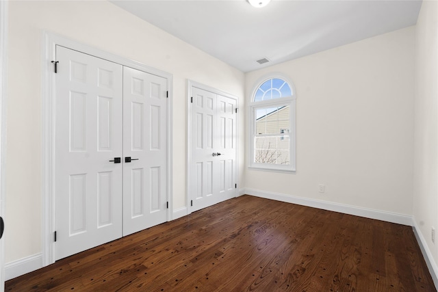 unfurnished bedroom with dark hardwood / wood-style floors and multiple closets