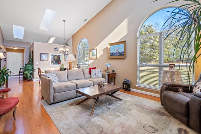 living room with a skylight, a healthy amount of sunlight, an inviting chandelier, and light wood-type flooring