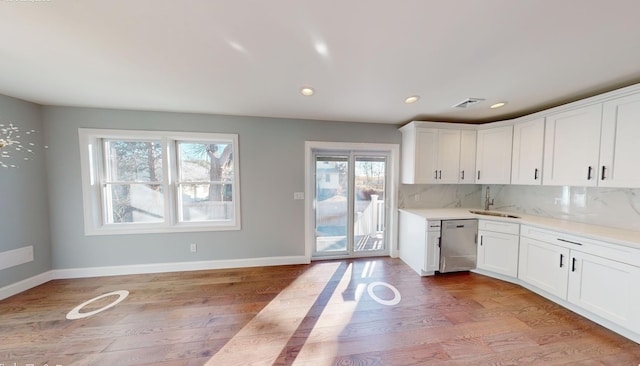 kitchen featuring stainless steel dishwasher, light hardwood / wood-style floors, white cabinetry, and backsplash