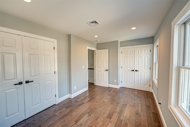 unfurnished bedroom featuring two closets, multiple windows, and wood-type flooring