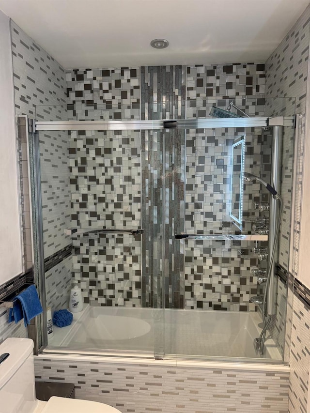 bathroom featuring toilet and bath / shower combo with glass door