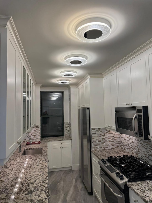 kitchen with sink, stainless steel appliances, light stone counters, backsplash, and white cabinets