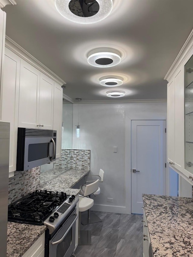 kitchen featuring light stone countertops, appliances with stainless steel finishes, backsplash, ornamental molding, and white cabinetry