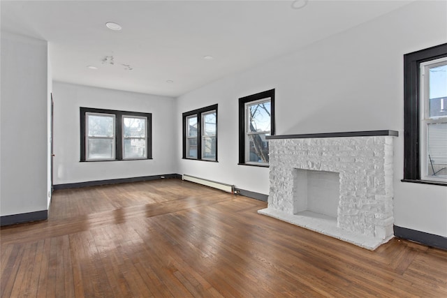 unfurnished living room featuring a fireplace with raised hearth, baseboards, baseboard heating, and wood finished floors