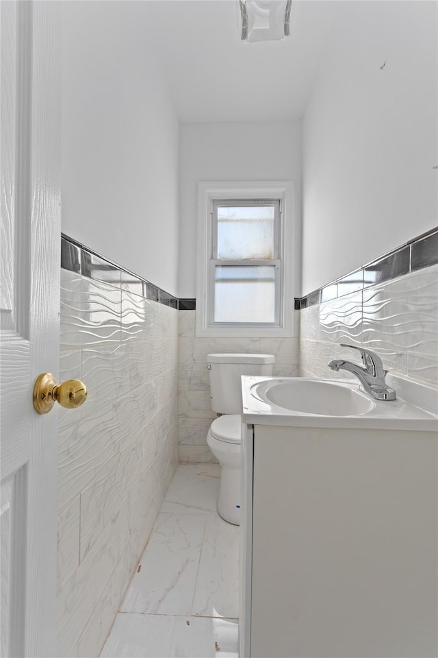 bathroom with toilet, vanity, tile walls, marble finish floor, and wainscoting