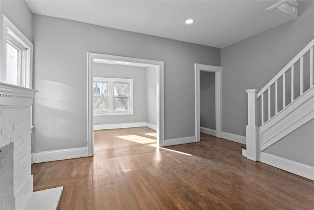 unfurnished living room featuring recessed lighting, wood finished floors, baseboards, stairs, and a brick fireplace