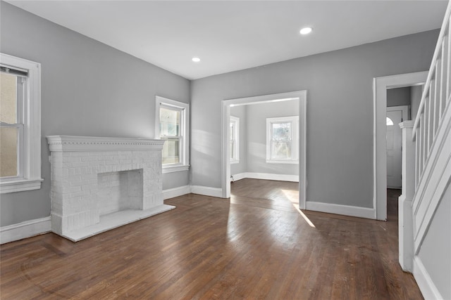 unfurnished living room featuring a healthy amount of sunlight, dark wood-style floors, stairs, and a fireplace