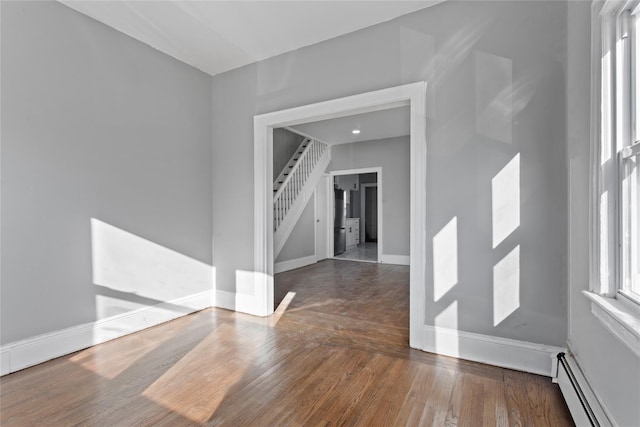 spare room with dark wood-type flooring, a baseboard radiator, baseboards, and stairs