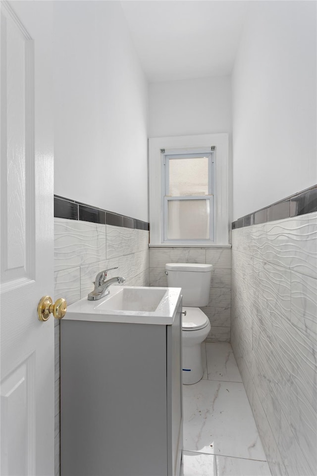 bathroom with toilet, a wainscoted wall, vanity, tile walls, and marble finish floor