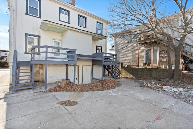 back of property featuring stairs, a chimney, and stucco siding