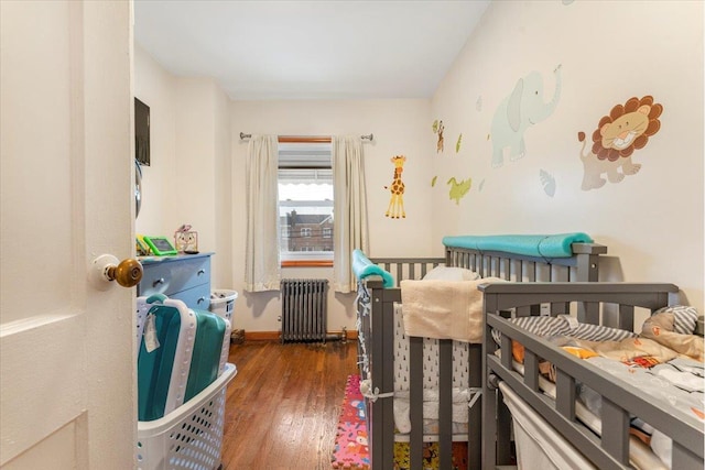 bedroom featuring radiator, dark wood-type flooring, and a crib