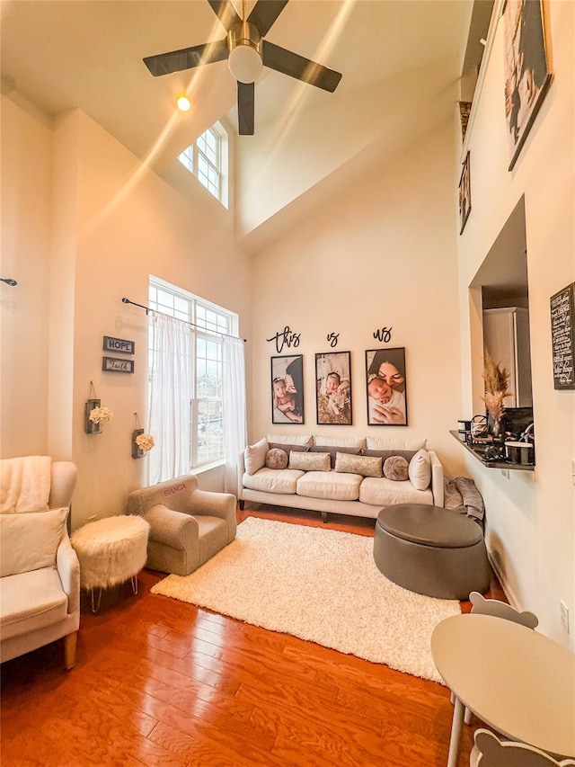 living room with ceiling fan, hardwood / wood-style floors, and a towering ceiling