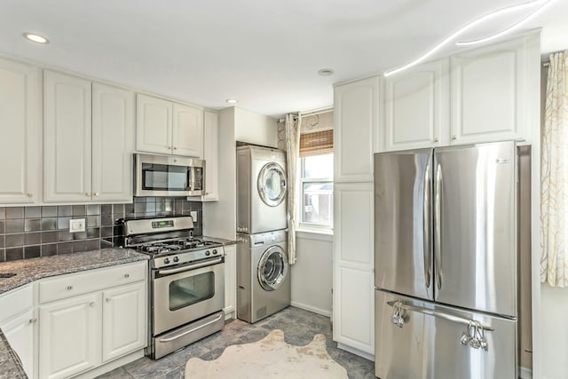 kitchen with appliances with stainless steel finishes, stacked washer and clothes dryer, dark stone countertops, and white cabinets