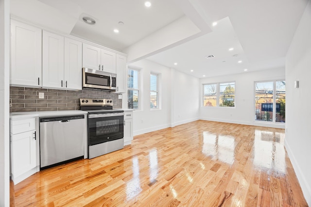 kitchen with stainless steel appliances, white cabinetry, light wood-type flooring, and backsplash