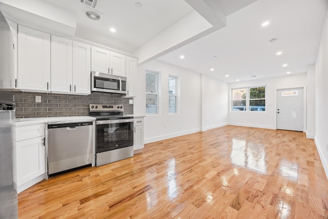 kitchen with appliances with stainless steel finishes, light wood-type flooring, white cabinets, and backsplash