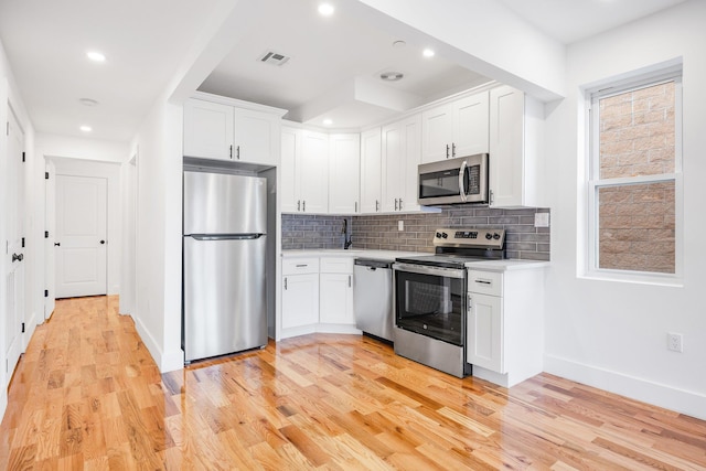 kitchen with appliances with stainless steel finishes, light hardwood / wood-style flooring, white cabinetry, and decorative backsplash