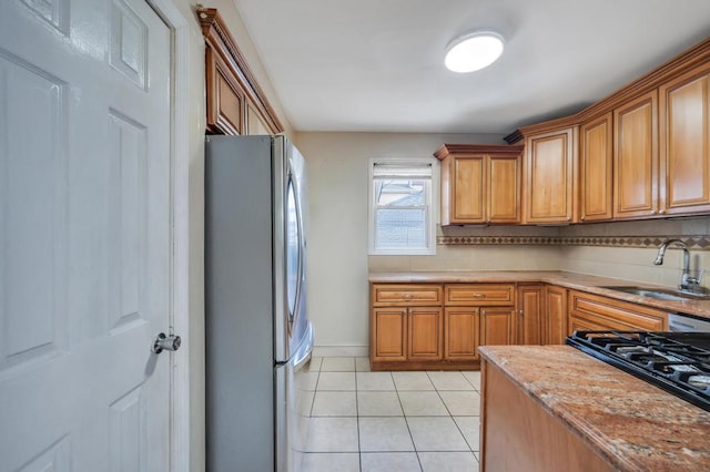 kitchen featuring brown cabinetry, light tile patterned flooring, a sink, and freestanding refrigerator