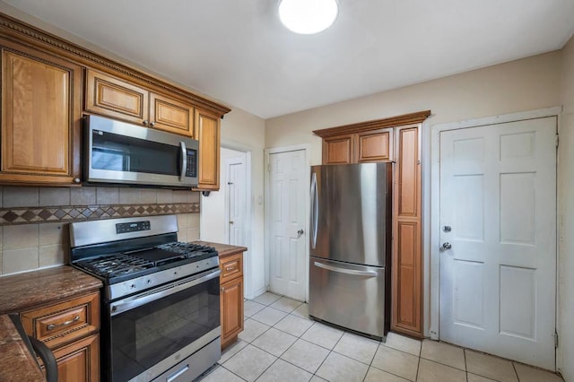 kitchen with light tile patterned floors, appliances with stainless steel finishes, decorative backsplash, and brown cabinets