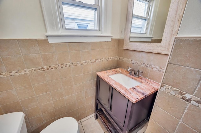 half bath featuring tile patterned flooring, vanity, toilet, and tile walls