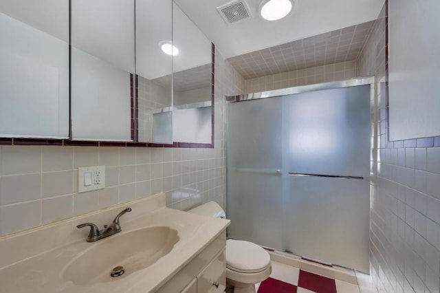 bathroom featuring visible vents, toilet, vanity, a shower stall, and tile walls