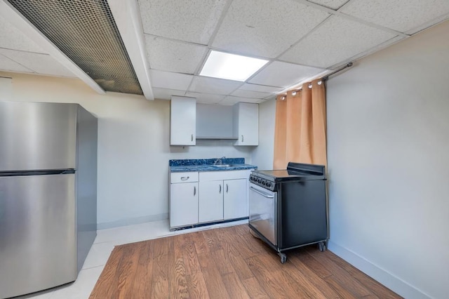 kitchen featuring dark countertops, freestanding refrigerator, white cabinets, a sink, and range