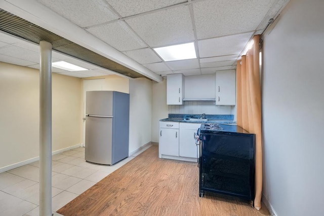 kitchen featuring a paneled ceiling, freestanding refrigerator, white cabinets, a sink, and light wood-type flooring