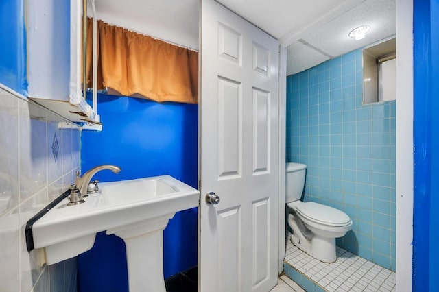 half bath featuring a sink, tile walls, toilet, and tile patterned floors