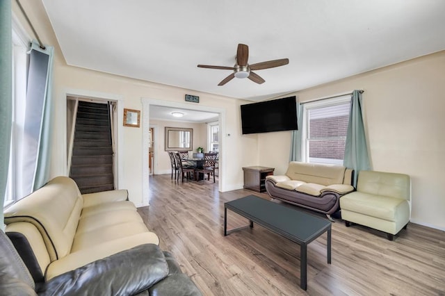 living area with a ceiling fan, plenty of natural light, stairway, and light wood finished floors